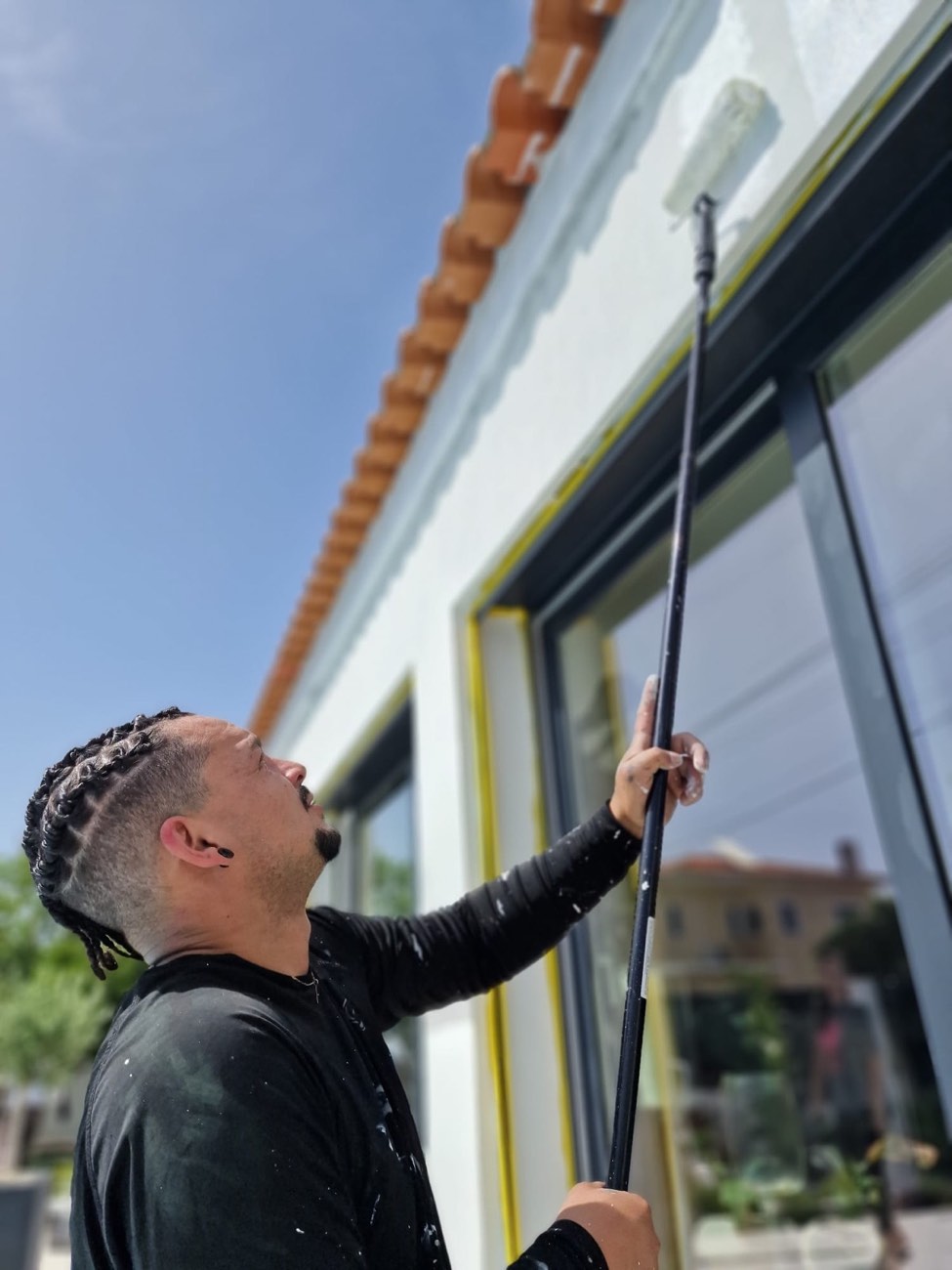 Pintor a pintar a fachada junto às janelas, com caixilhos protegidos