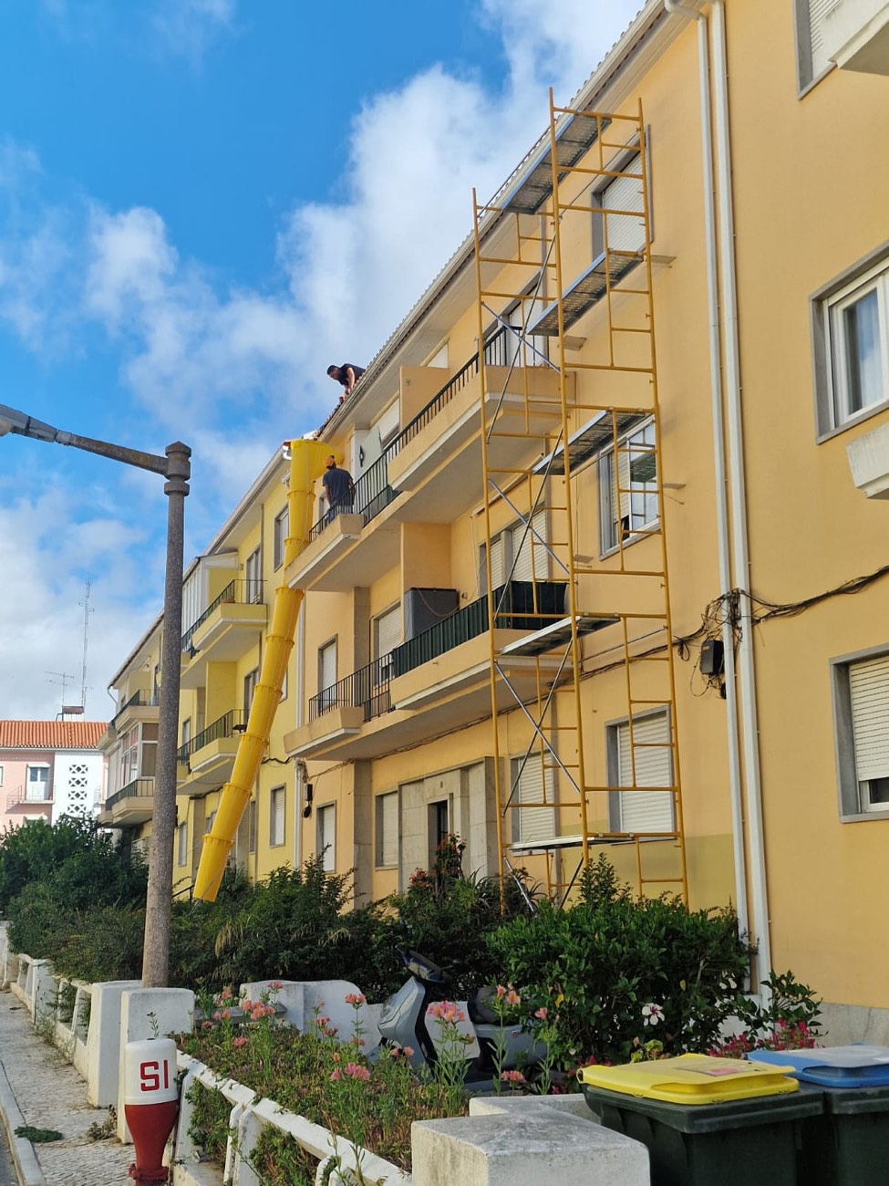 Prédio amarelo de três andares com andaime para pintura da fachada